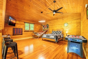 Un interior de madera con una cama, mesa de fútbol, hamaca y televisor.
