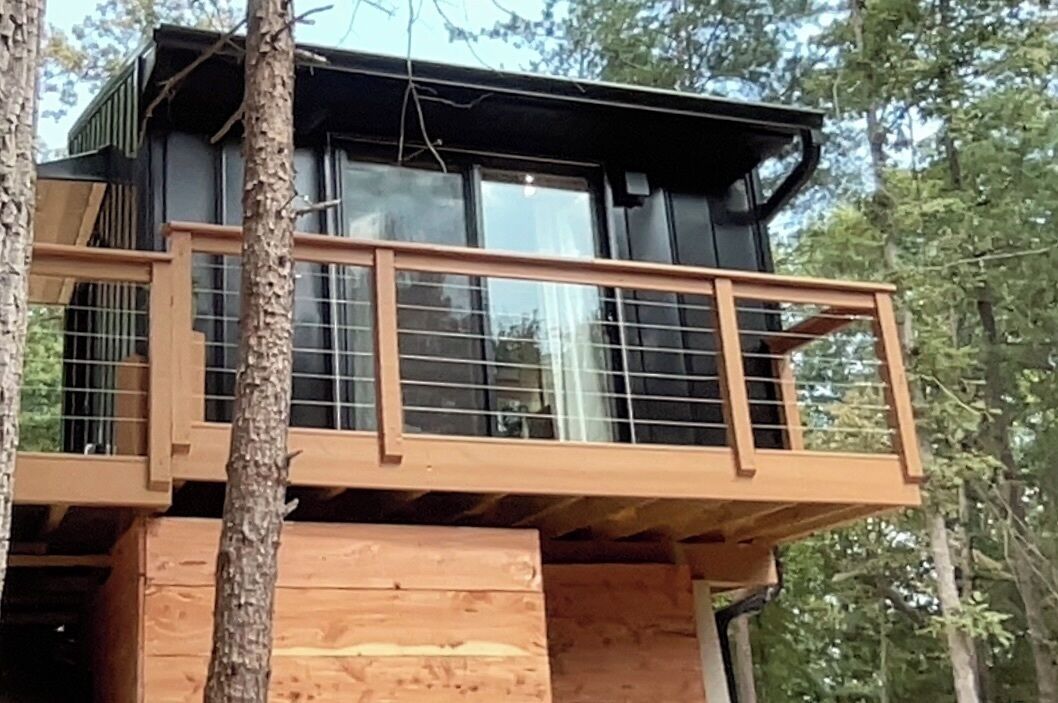 A modern wooden cabin with a balcony, surrounded by trees.
