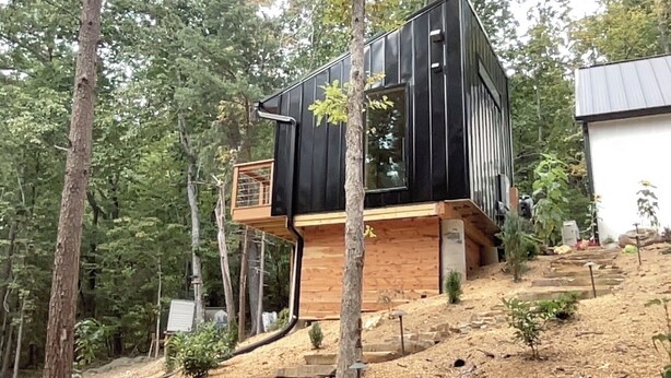 Eine moderne Holzhütte mit einer Holzdiele und schwarzem Anstrich, umgeben von Bäumen.