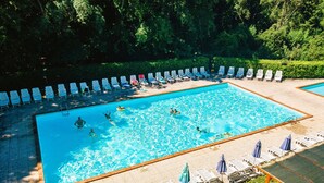 Ein rechteckiger Pool, umgeben von Liegestühlen und Sonnenschirmen, mit badenden und spielenden Personen im Wasser.