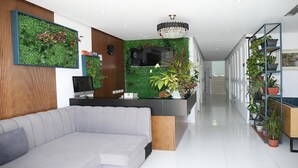 A modern reception area with a sofa, a reception desk, a TV, and a green wall with plants. - Pashkaj Hotel (Udënisht)