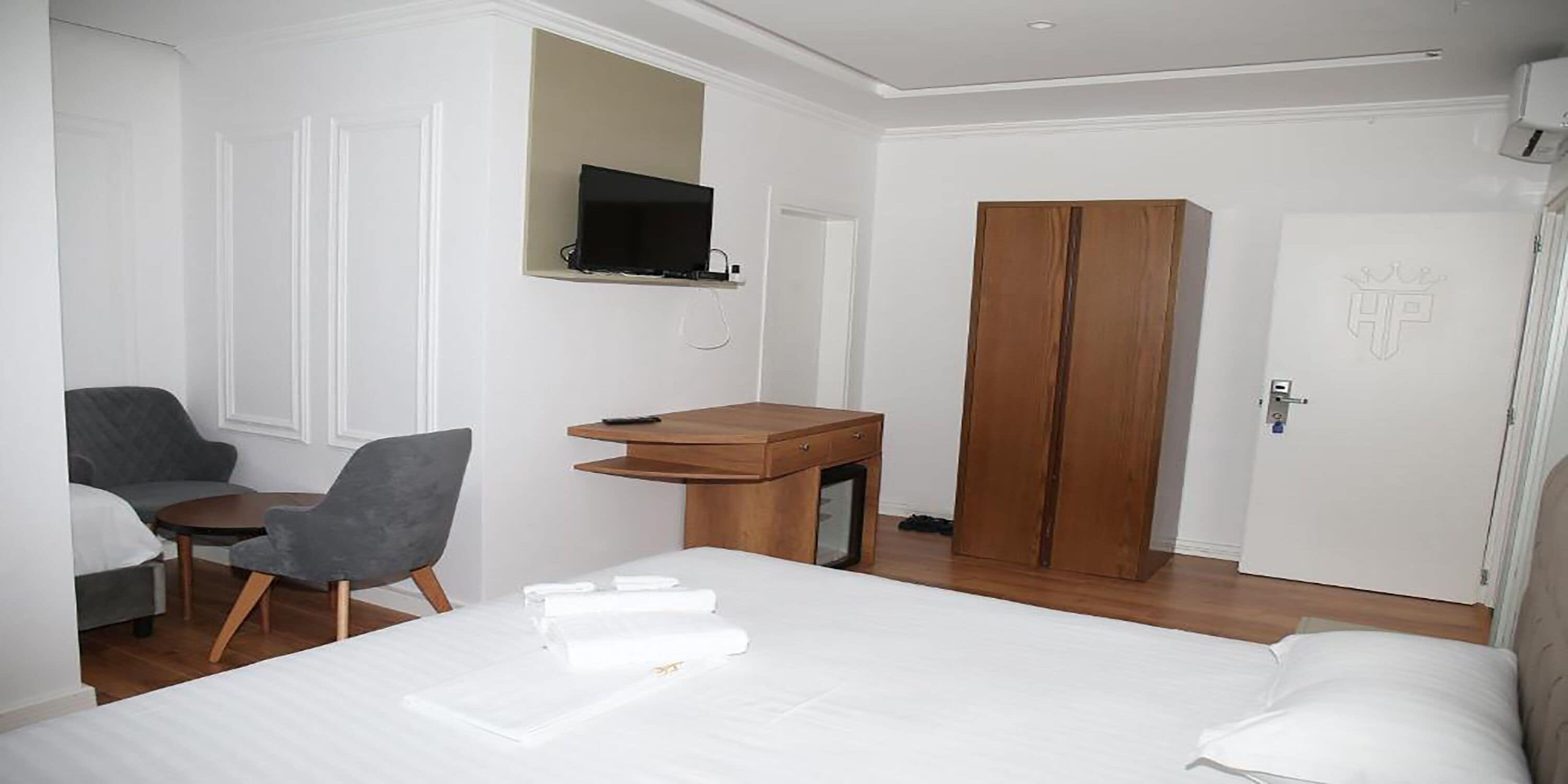 Una habitación de hotel con cama, escritorio con silla, televisor montado en la pared y armario.