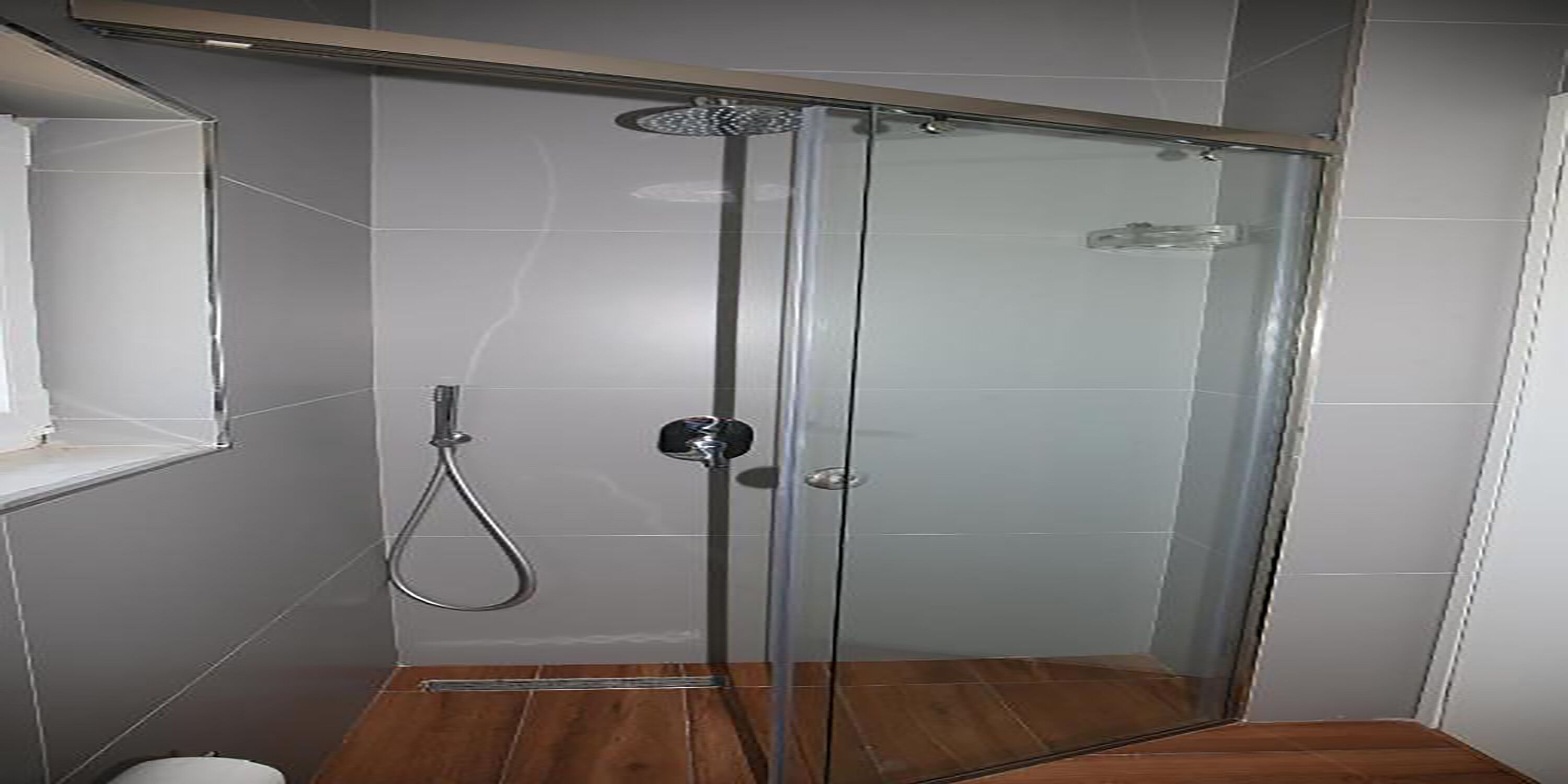 A glass-enclosed shower with a handheld showerhead, a wall-mounted control panel, and a wooden floor.