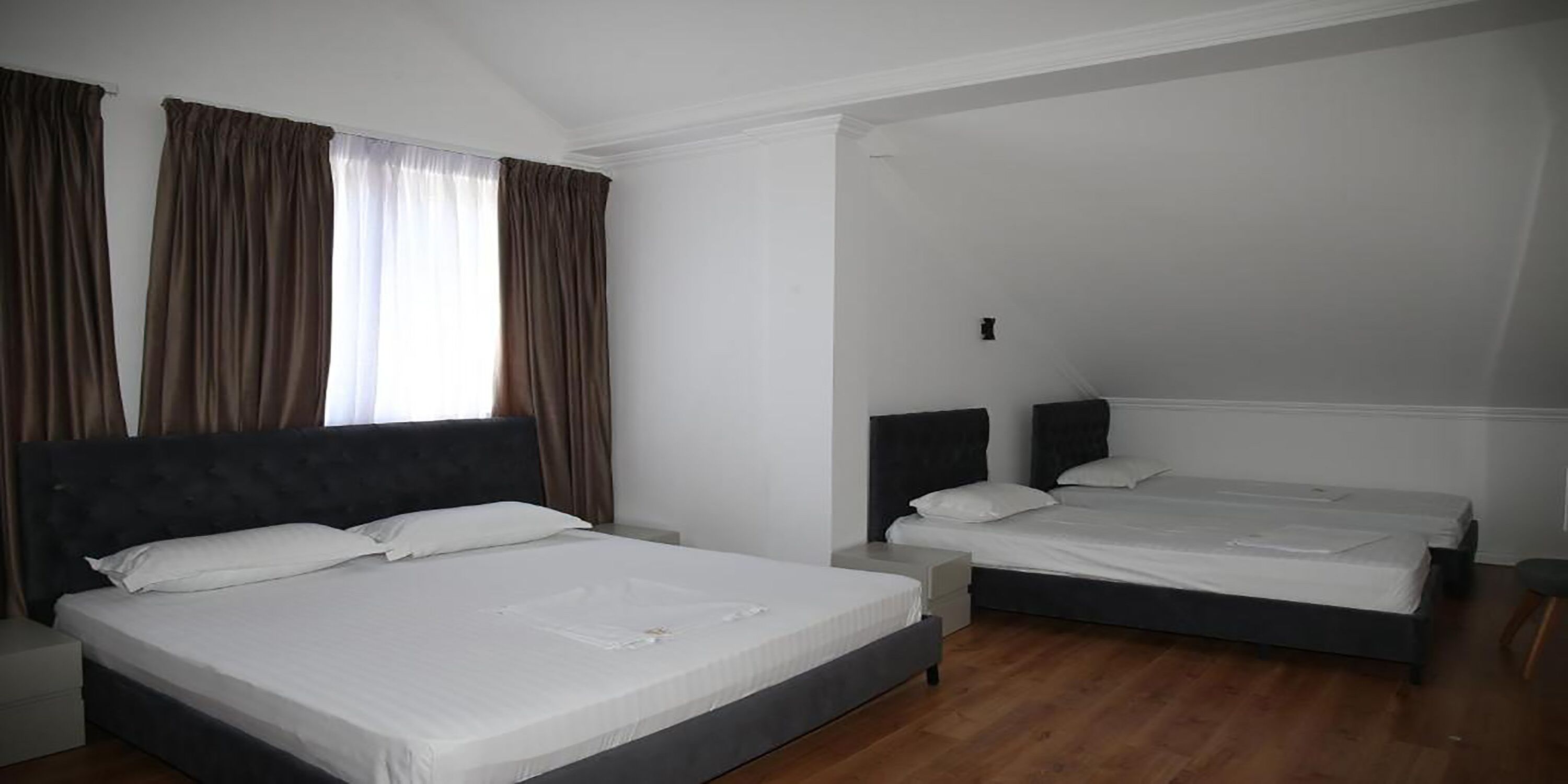 Un dormitorio con dos camas, una ventana con cortinas y suelo de madera.