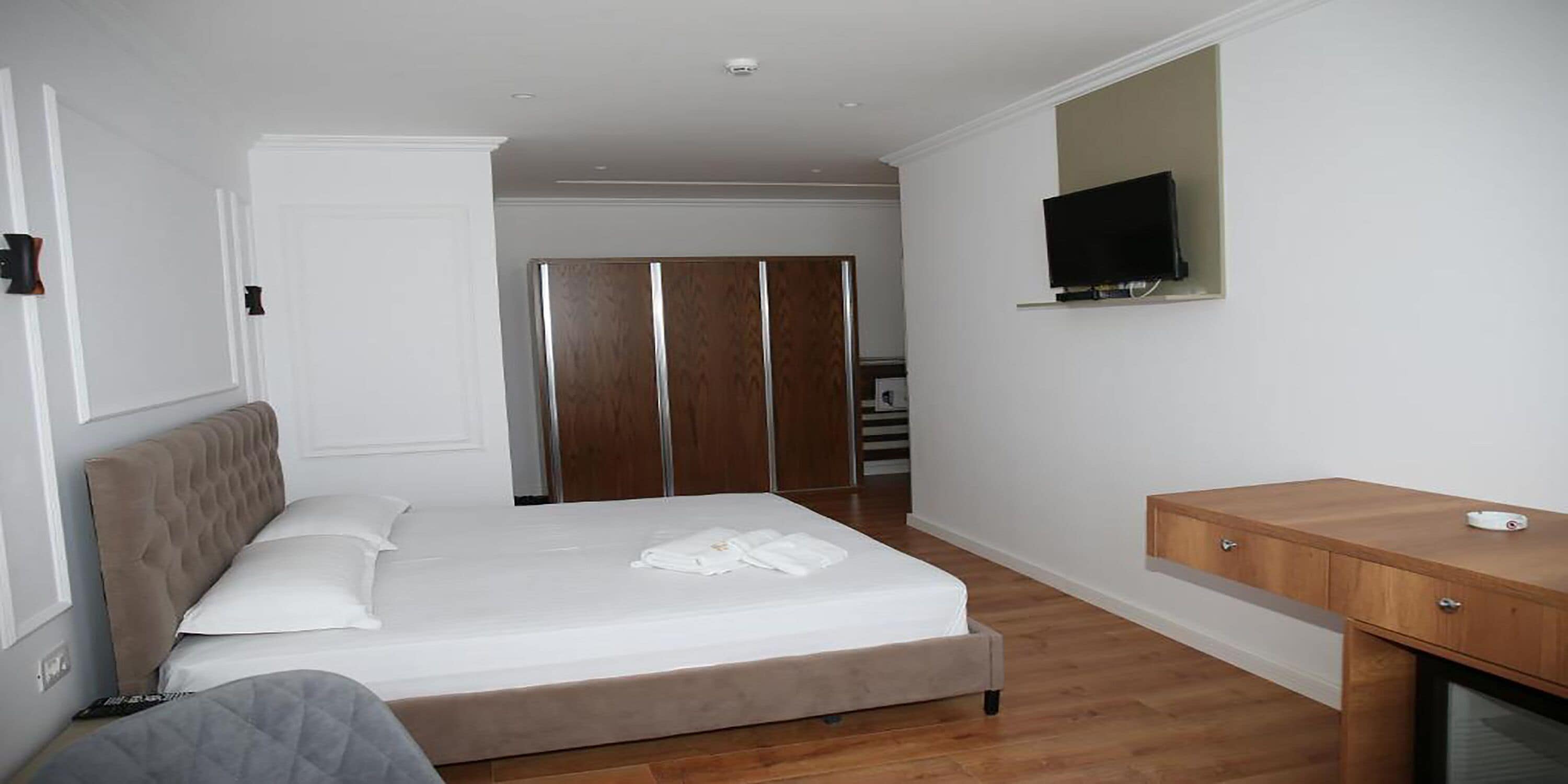 Una camera da letto con un letto, un armadio in legno, una TV a parete e una scrivania in legno.