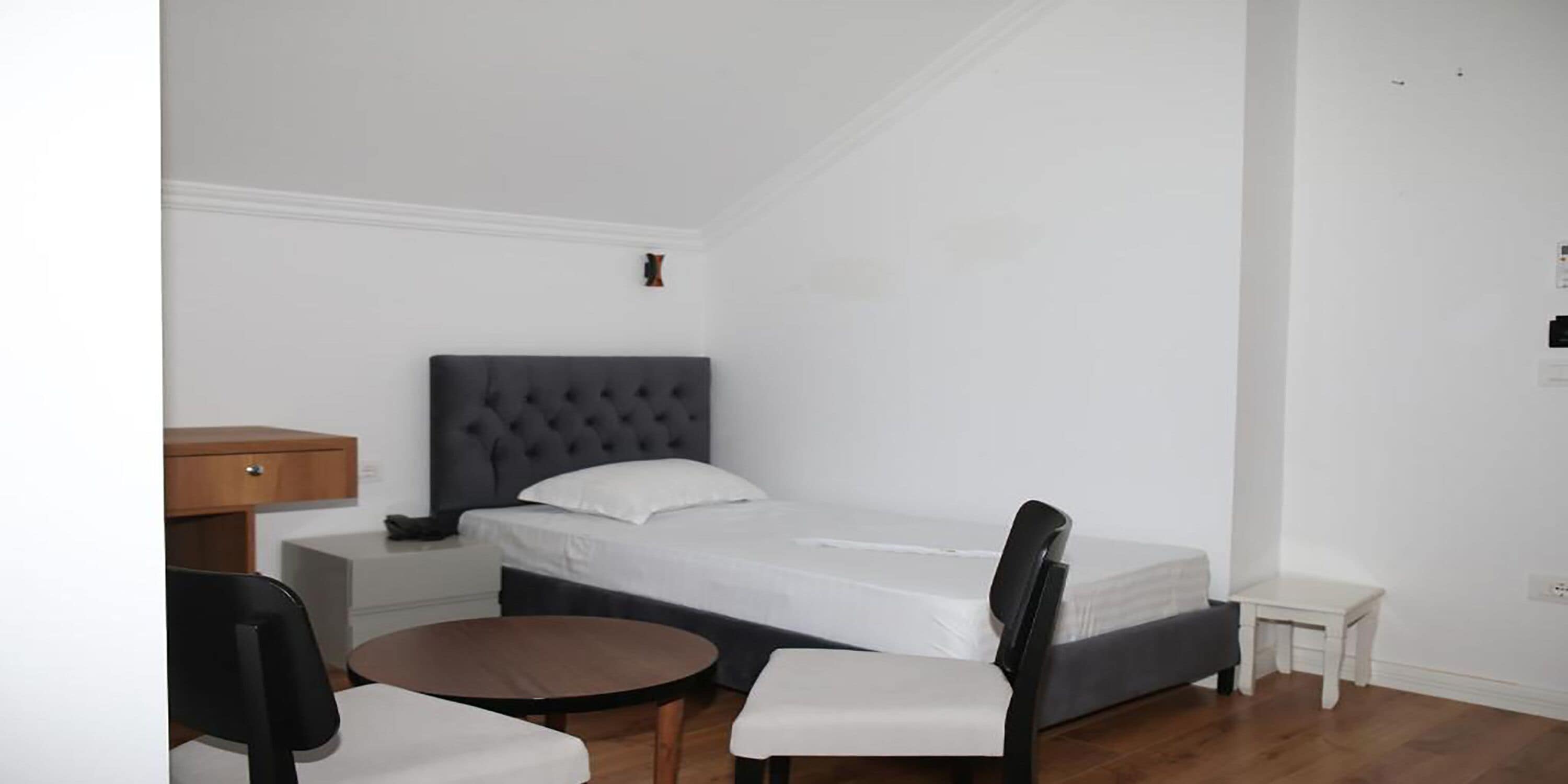 Une petite chambre à coucher, bien rangée, avec un lit simple, une table de chevet, une chaise et une petite table ronde.