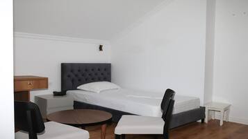 Une petite chambre à coucher, bien rangée, avec un lit simple, une table de chevet, une chaise et une petite table ronde.