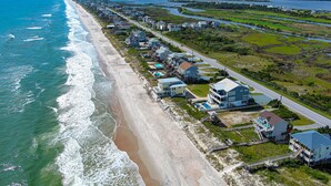 Vista aérea de una zona residencial costera con casas a lo largo de la playa y una carretera que sigue la costa.