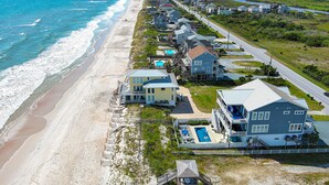 Una zona residencial costera con casas frente a la playa, una carretera y una piscina.