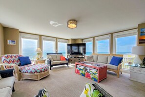 Un salon spacieux doté d’un grand téléviseur à écran plat, de sièges confortables et de grandes fenêtres offrant une vue sur l’océan.