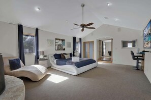 A spacious bedroom with a large bed, a curved sofa, a ceiling fan, and a desk with a chair.