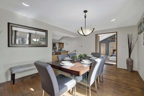 A modern dining area with a wooden table, grey upholstered chairs, and a hanging light fixture.