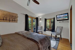 Une chambre à coucher avec un lit, une télévision, un tableau et une fenêtre avec des rideaux.