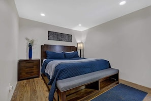 A bedroom with a bed, bedside table, lamp, and a wall-mounted artwork.