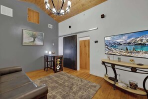 A living room with a sofa, a TV mounted on the wall, a wooden ceiling, and a painting of a tree.