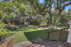A backyard with a wooden deck, a stone pathway, and a grassy area with trees.