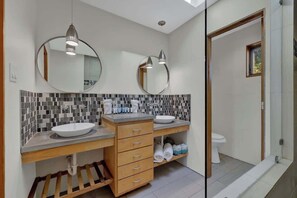 Une salle de bain moderne avec deux lavabos, un miroir et un espace douche.