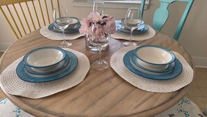 A round wooden dining table set with blue and white plates, clear wine glasses, and a vase with pink flowers. - Cozy Camellia Cottage – Minutes to Downtown & Augusta National (Augusta)