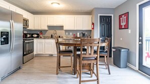 A modern kitchen with white cabinets, stainless steel appliances, and a wooden dining table. - Memorial Field Lodge - 4 Bd Townhome by IU Sports (Bloomington)