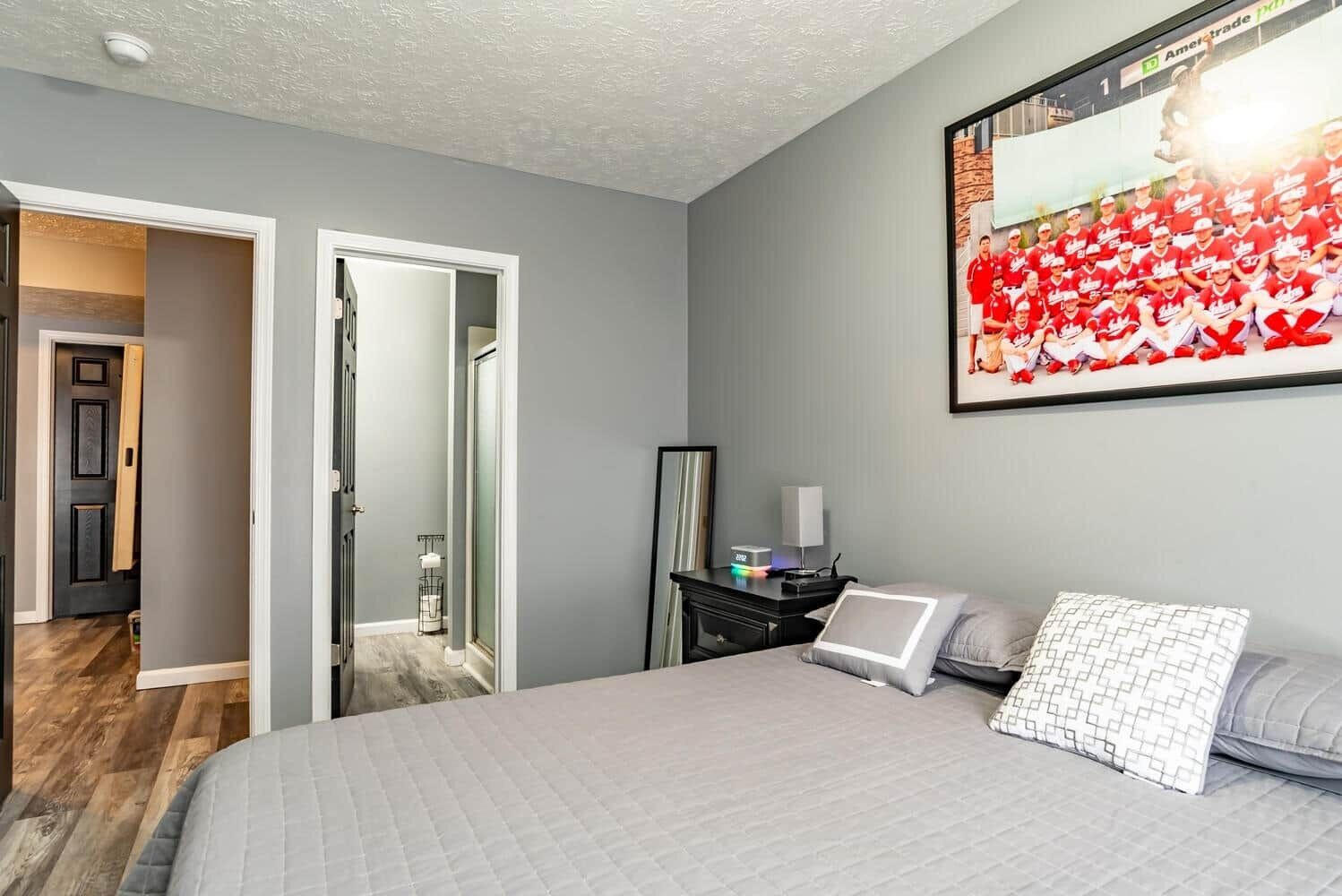 A bedroom with a bed, bedside table, lamp, and a large framed picture on the wall.