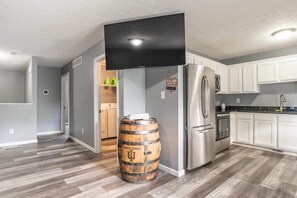 Una cocina moderna con un refrigerador de acero inoxidable, un televisor de pantalla plana montado arriba y un barril de madera en el centro.