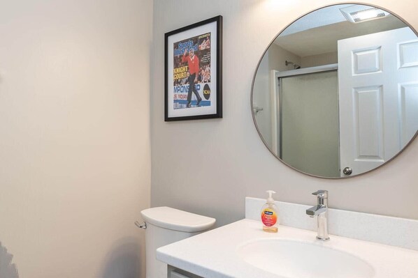 A bathroom with a white toilet, a sink with a soap dispenser, and a framed sports magazine on the wall.