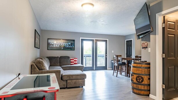 A living room with a sofa, a coffee table, a TV mounted on the wall, and a wooden barrel. - IU Soccer Hideaway - 4 Bd Townhome by IU Sports (Bloomington)