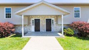 A two-story house with a covered front porch, two doors, and a stone foundation. - IU Soccer Hideaway - 4 Bd Townhome by IU Sports (Bloomington)