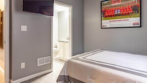 A hotel room with a bed, a flat-screen TV mounted on the wall, and a framed photo of a soccer team on the wall. - IU Soccer Hideaway - 4 Bd Townhome by IU Sports (Bloomington)