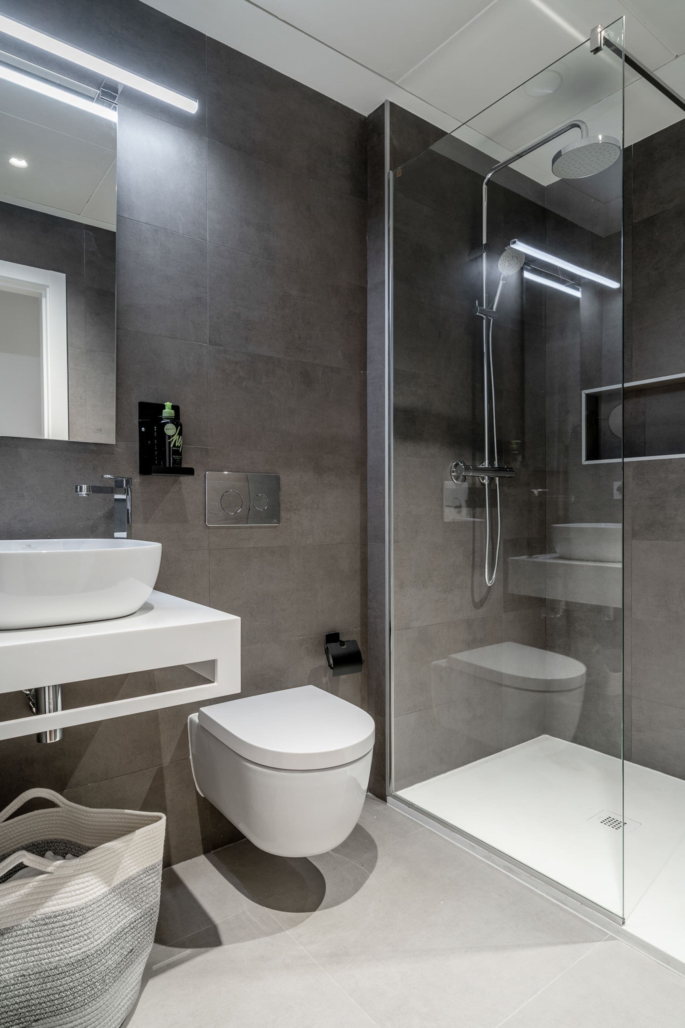 Un baño moderno con ducha envuelta en vidrio, lavamanos blanco y retrete.