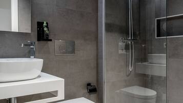 Un baño moderno con ducha envuelta en vidrio, lavamanos blanco y retrete.