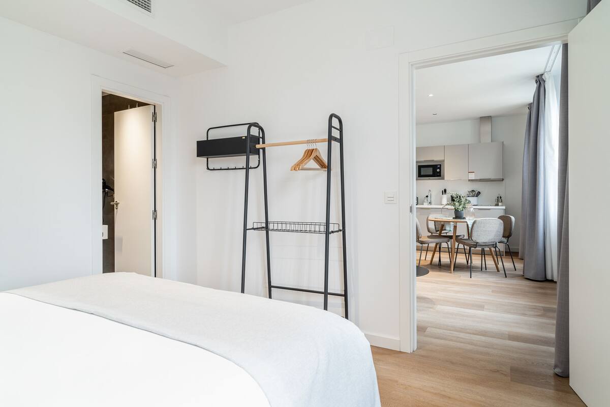 Une chambre d’hôtel moderne, équipée d’un lit, d’une étagère en métal noir, d’un cintre en bois et offrant une vue sur la salle à manger.