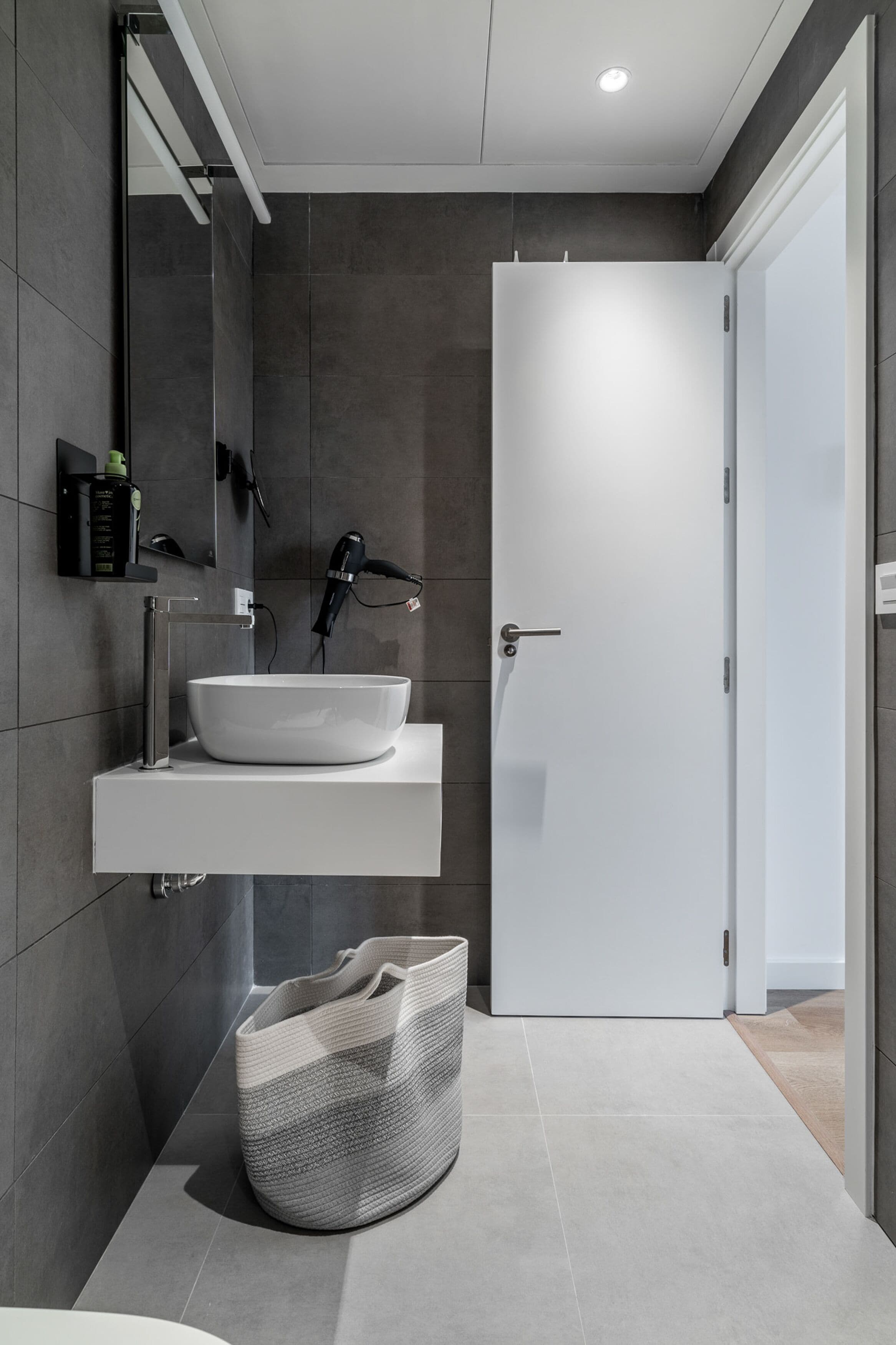 A modern bathroom with a white sink, a towel rack, and a hairdryer on the wall.