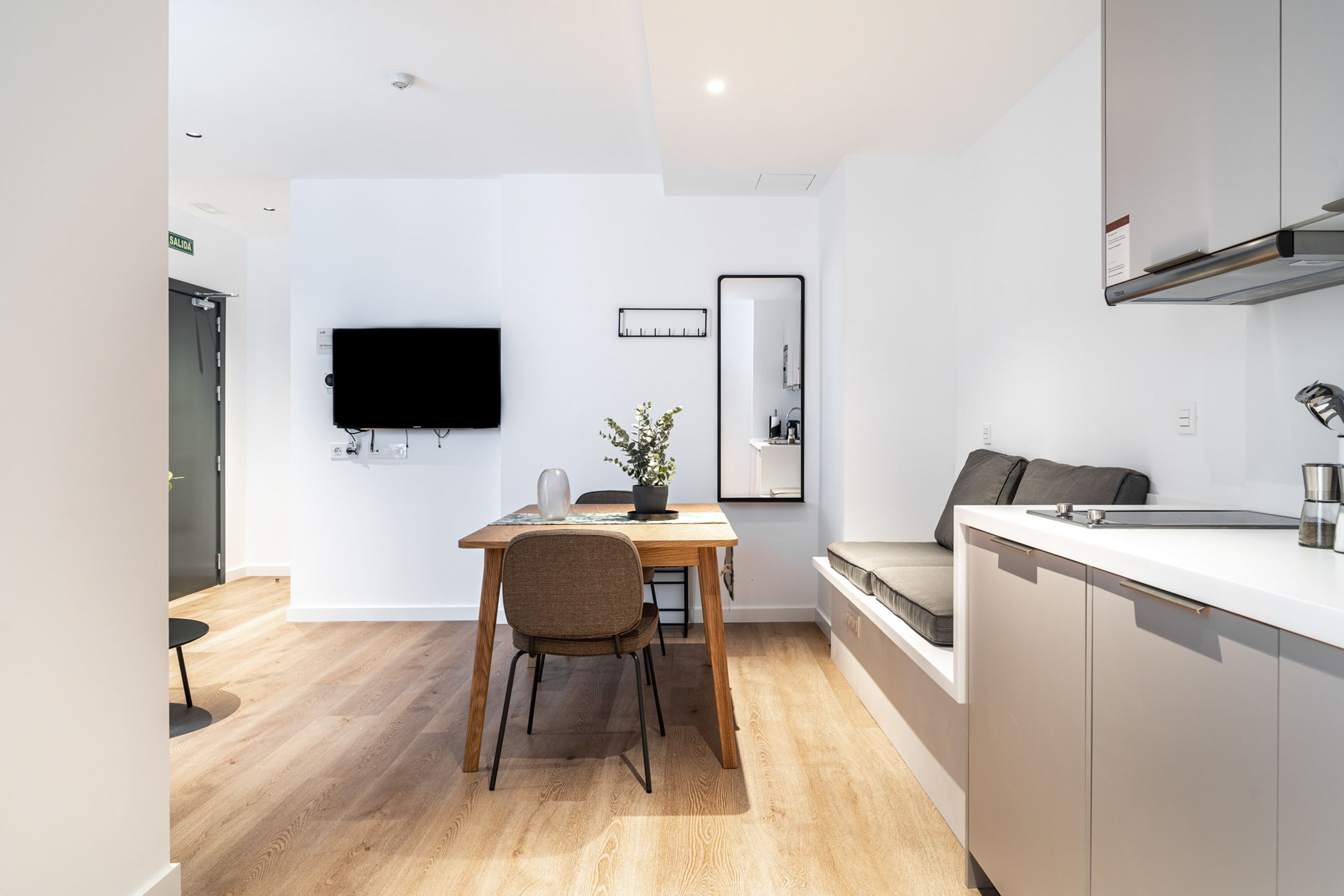 Una cocina moderna con una mesa de madera, una silla, una planta en maceta, un televisor de pantalla plana y un espejo grande.