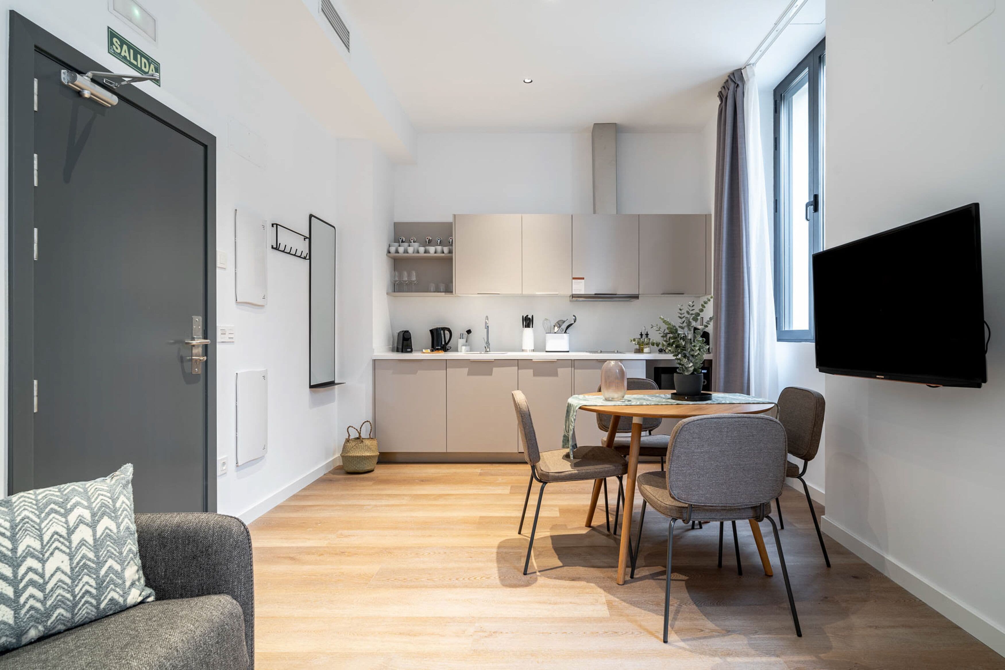 A modern kitchen with a dining area, a flat-screen TV mounted on the wall, and a door labeled "SALIDA".