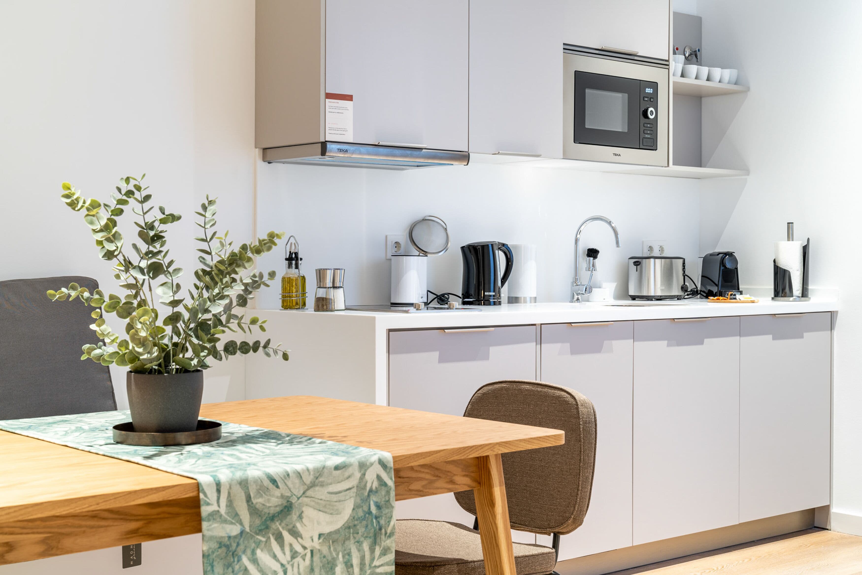 A modern kitchen with white cabinets, a microwave, a kettle, and a coffee machine.