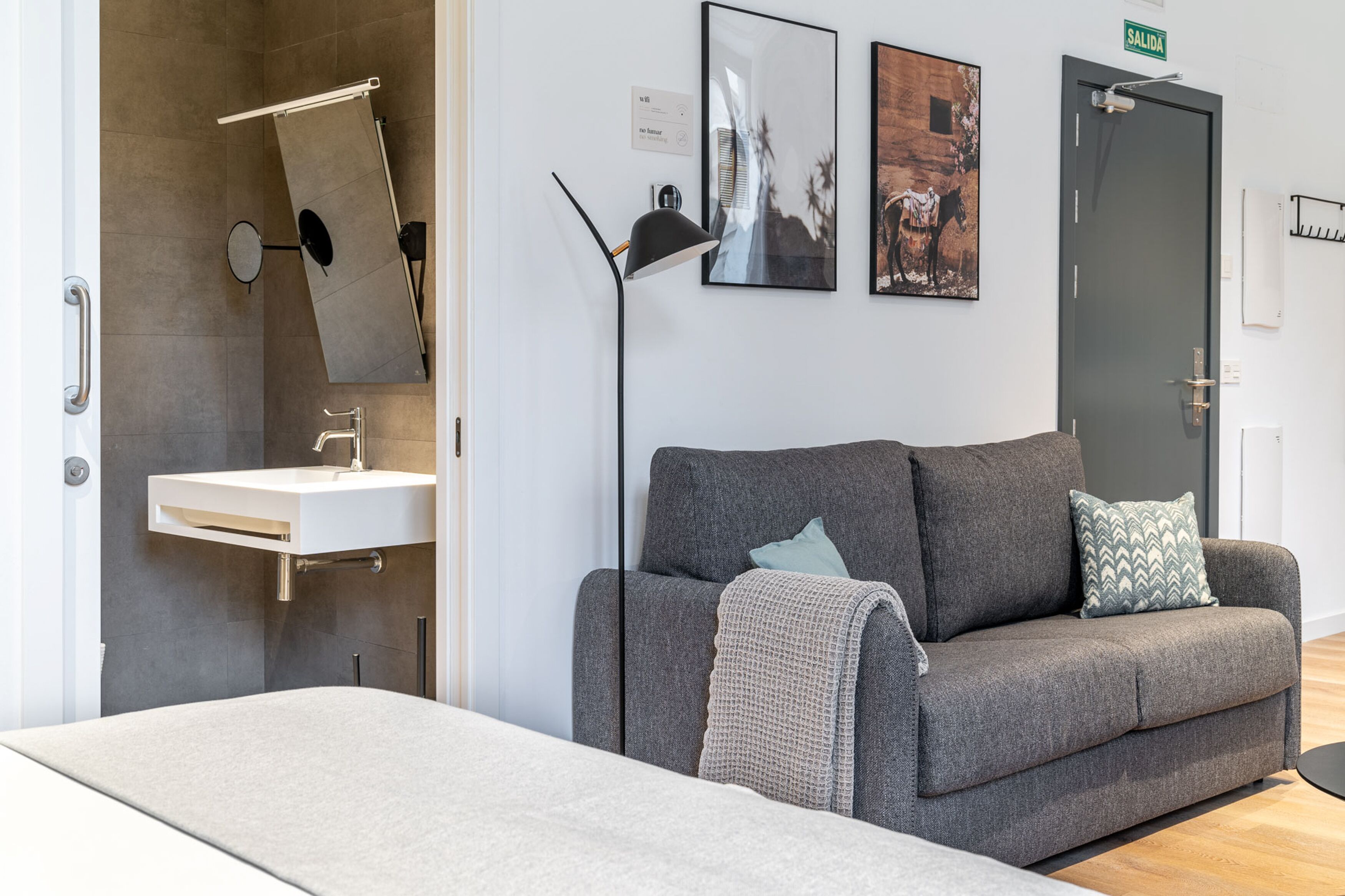 A modern room with a grey sofa, a white sink, and a door labeled "SALIDA".