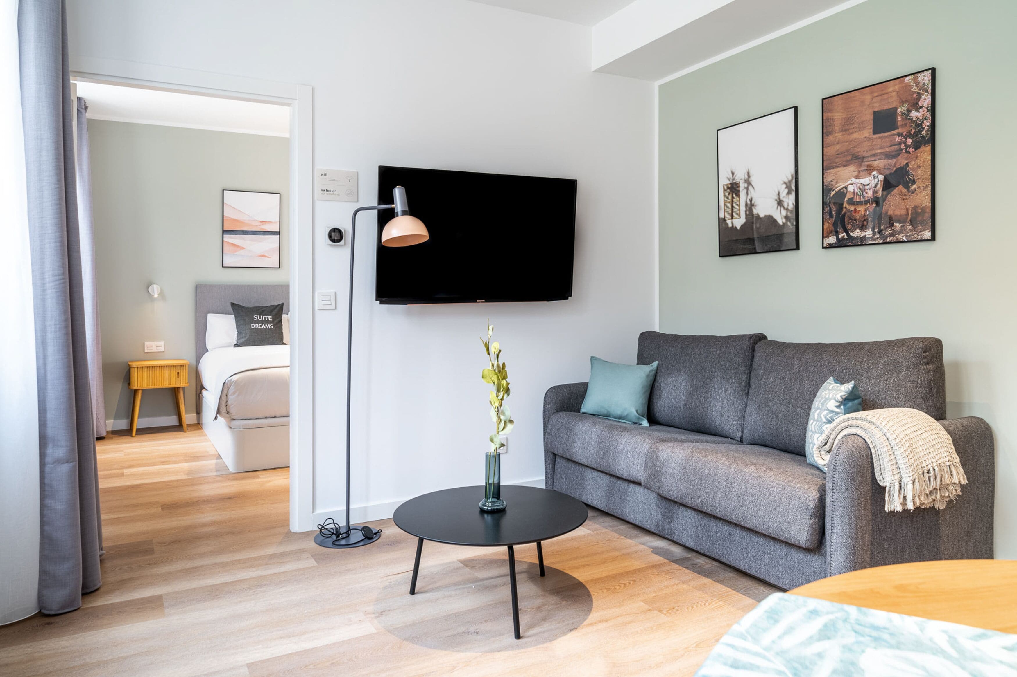 Una sala de estar moderna con un sofá gris, una mesa de centro negra y un televisor de pantalla plana montado en la pared.