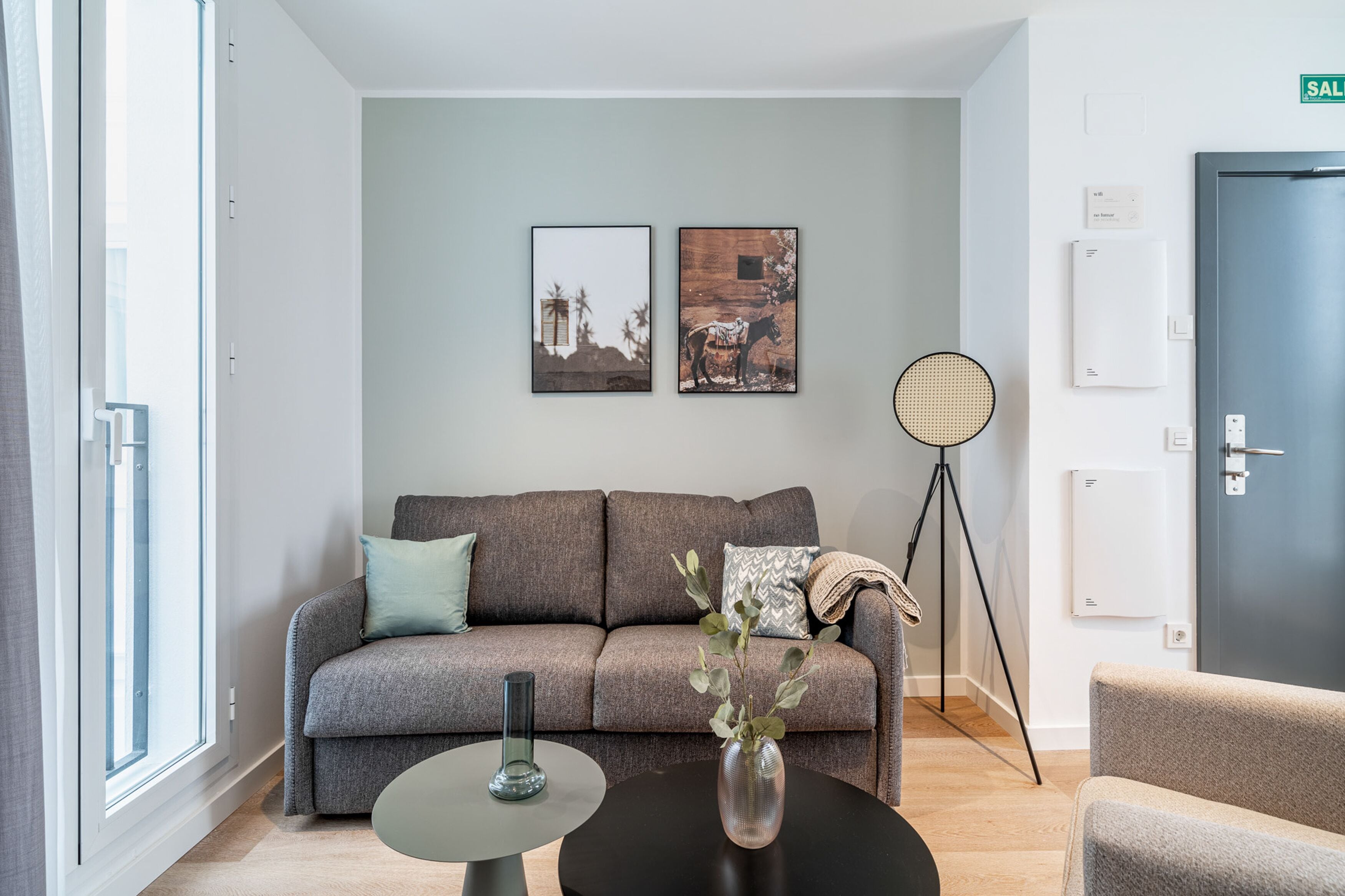 Ein modernes Wohnzimmer mit einem grauen Sofa, einem runden Tisch mit einer Vase und einer Stehlampe.