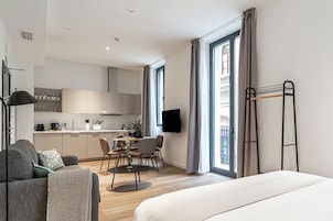 Une chambre d’hôtel moderne comprenant un lit, un canapé, une table à manger avec des chaises, un coin cuisine et un balcon avec des rideaux.
