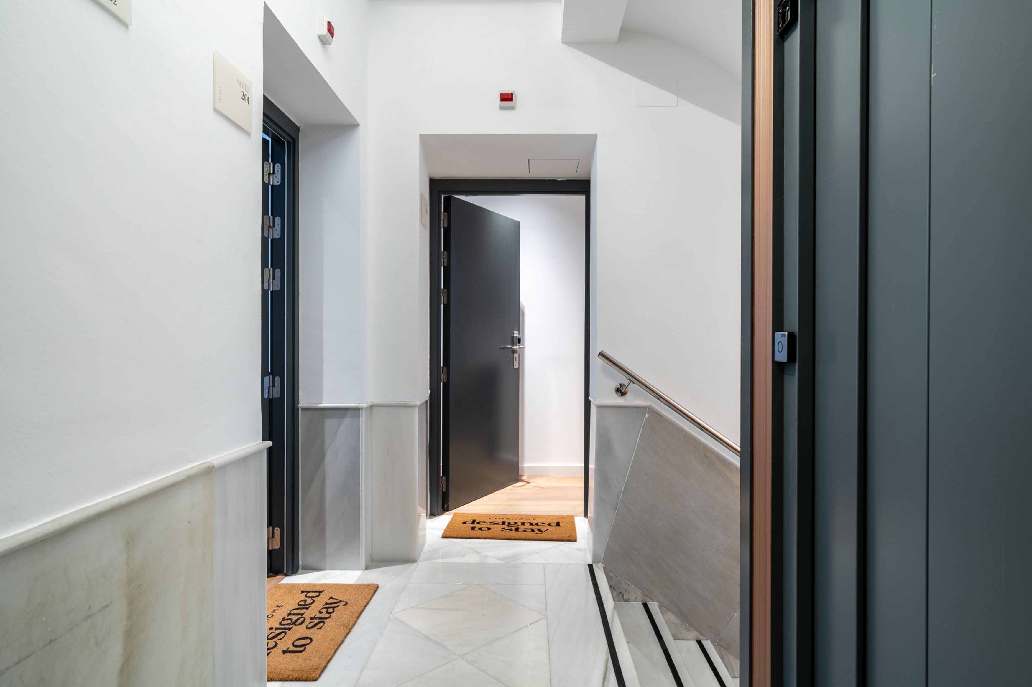 A hallway with a door at the end, a doormat, and a handrail on the right.