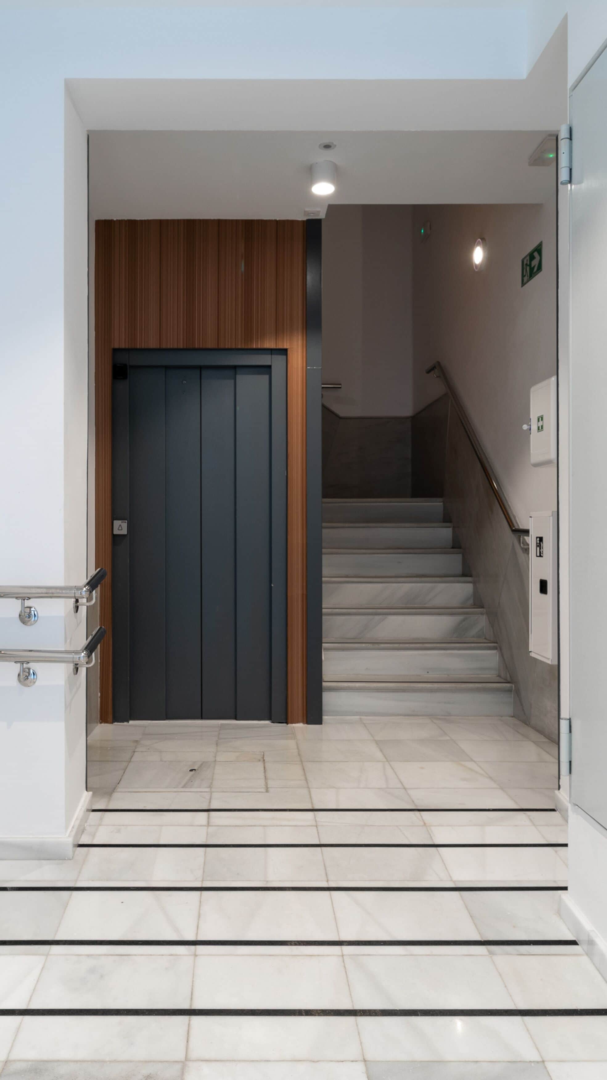Ein modernes Interieur mit einer dunklen Tür, einer Wand aus Holzpaneelen und einer Treppe, die in einen oberen Bereich führt.