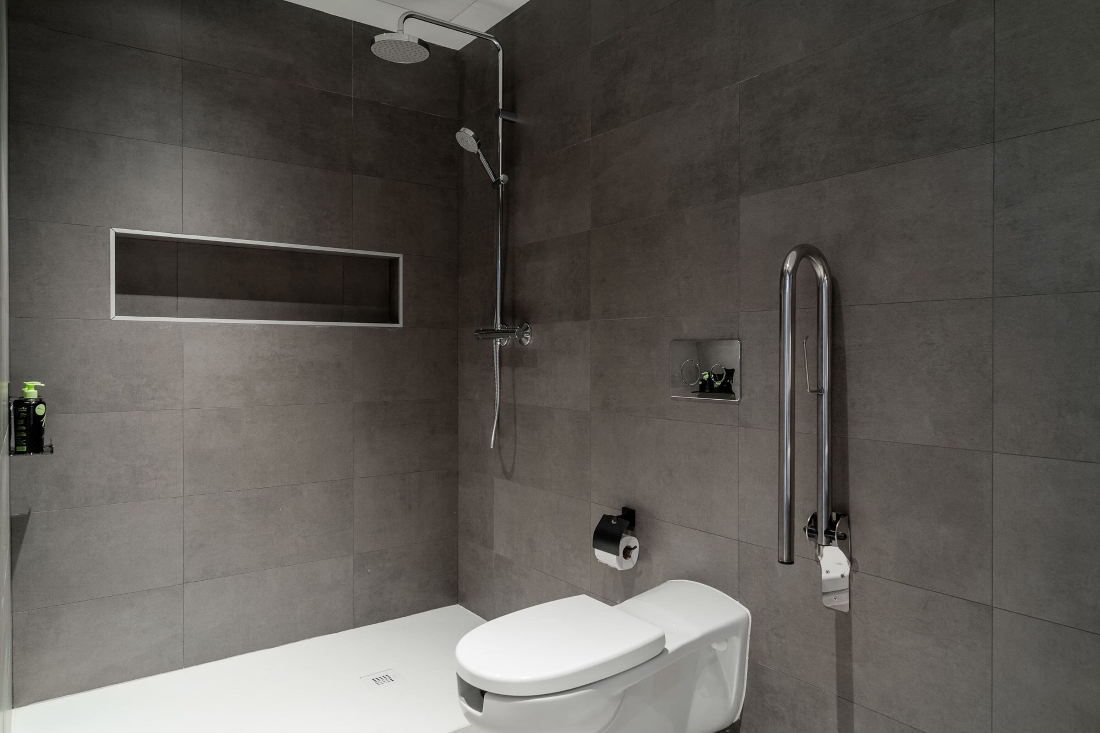 A modern bathroom with a shower, toilet, and a shelf with toiletries.