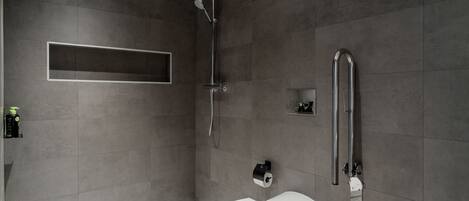 A modern bathroom with a shower, toilet, and a shelf with toiletries.