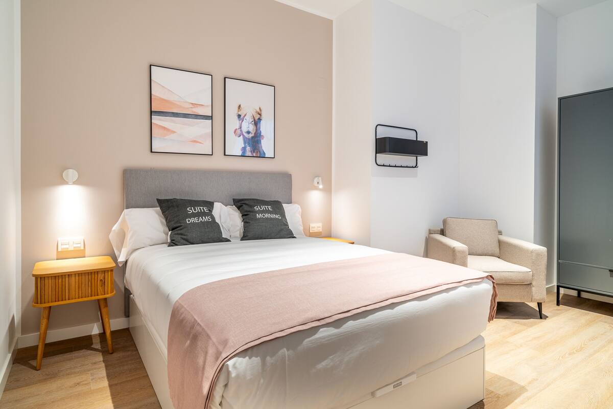 Une chambre moderne avec un grand lit, deux oreillers, une table de chevet, une chaise et une armoire.