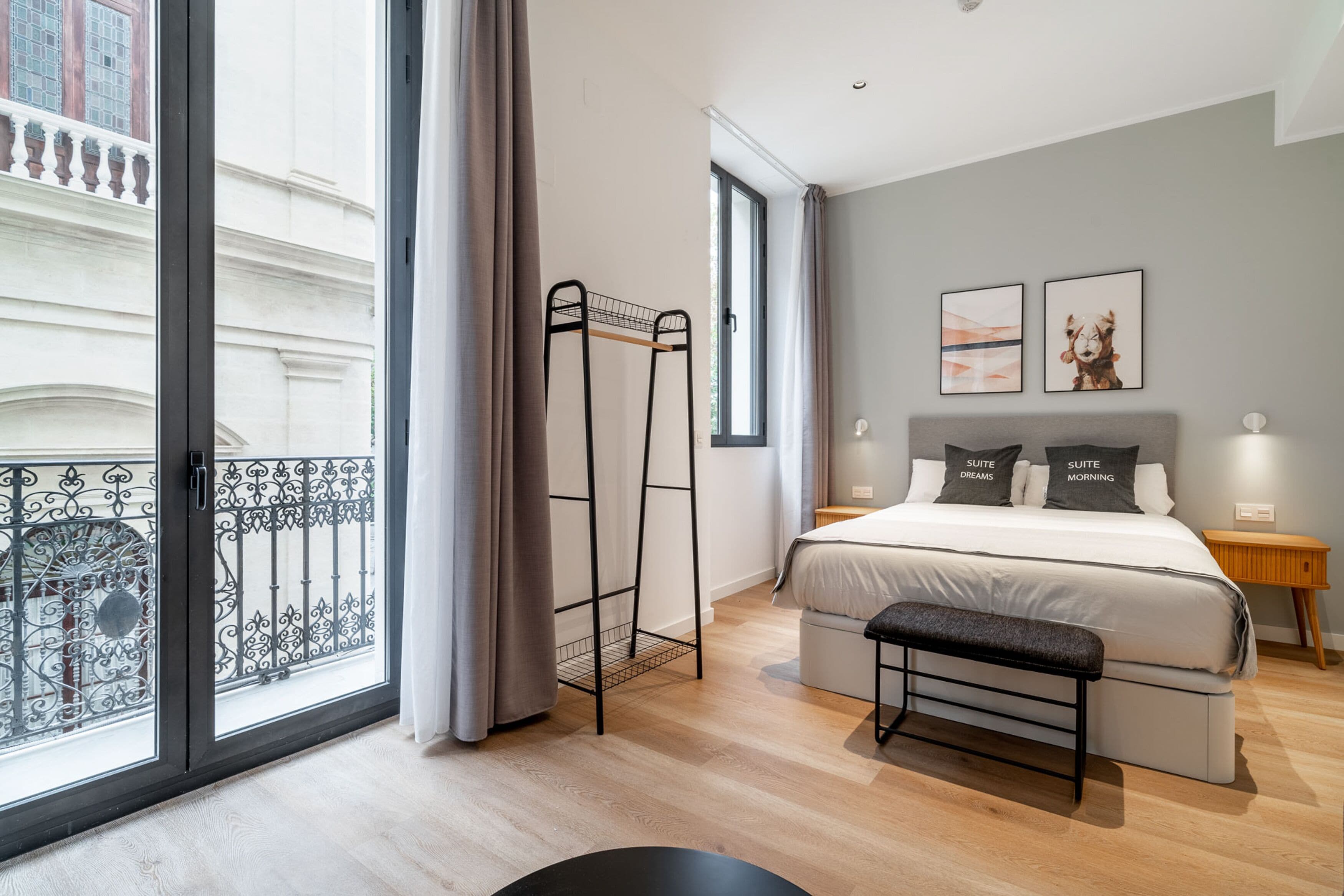 A modern bedroom with a large window, a bed with matching pillows, a bench, and a nightstand.