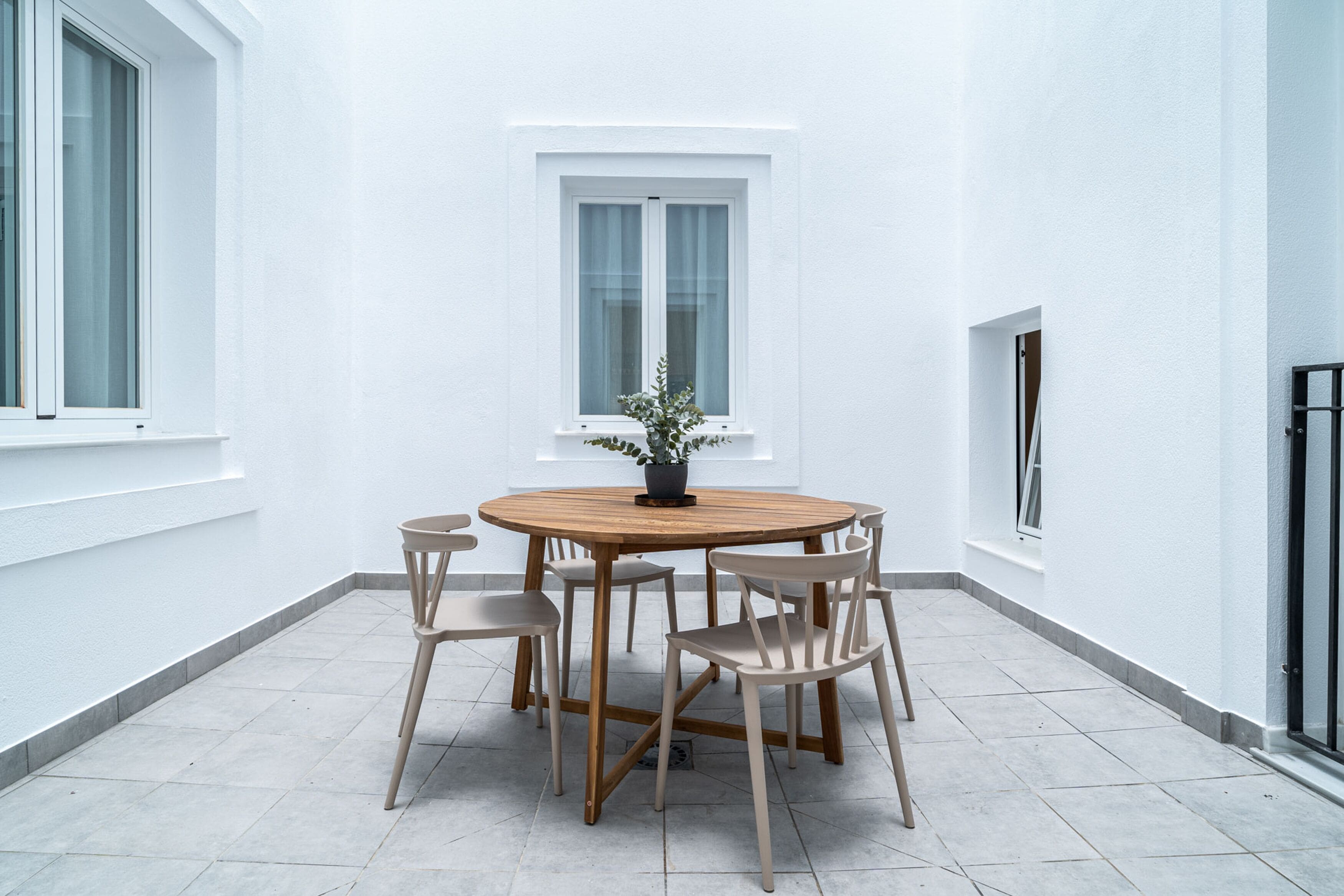 Una mesa redonda de madera con seis sillas, una planta en maceta y una ventana con cortinas blancas.