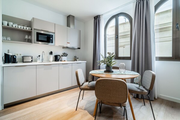 Una cocina moderna con armarios blancos, un microondas y un comedor con una mesa redonda y dos sillas.