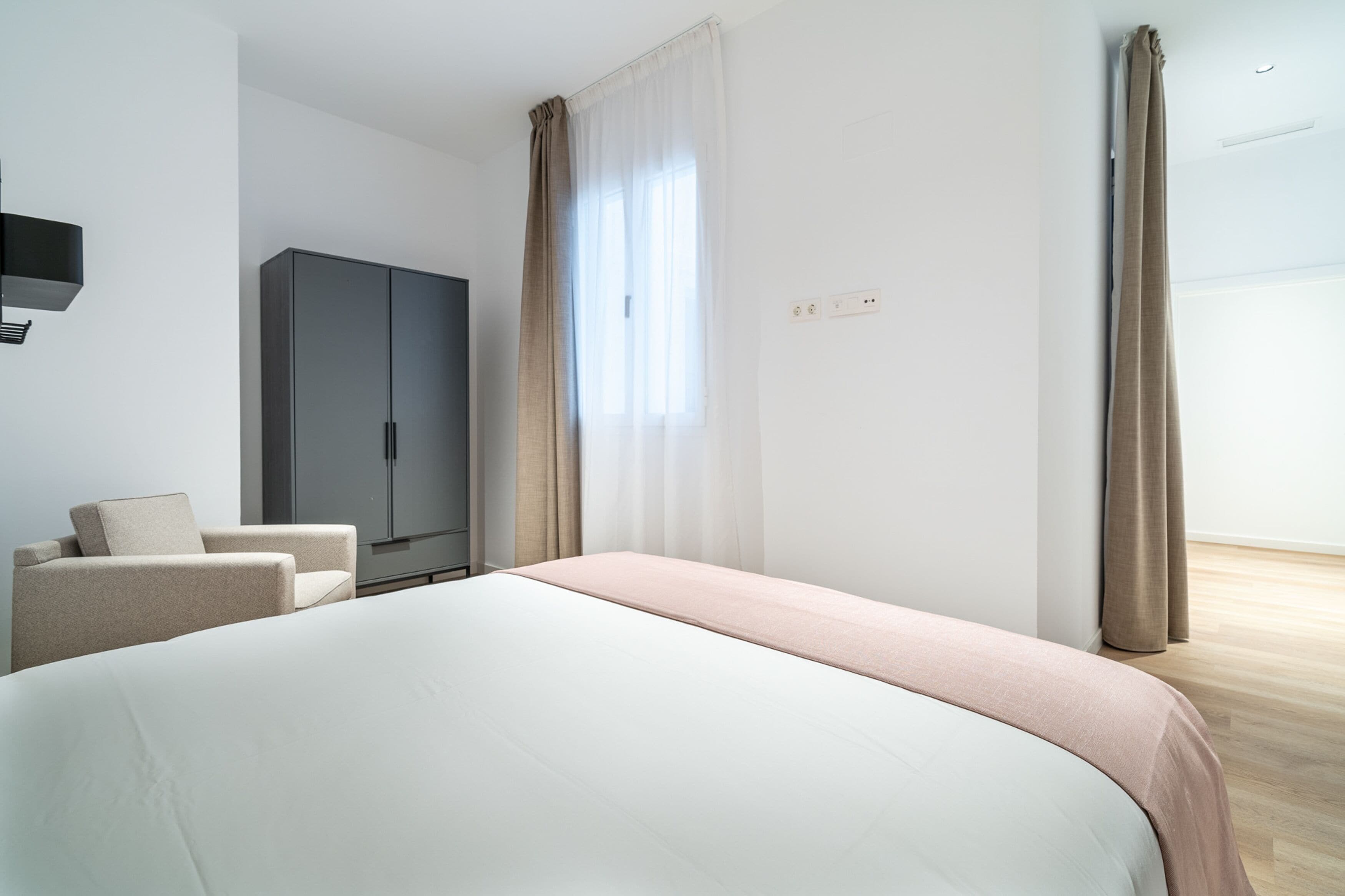 Une chambre d’hôtel moderne dotée d’un grand lit, d’une armoire, d’un coin salon et d’une fenêtre avec des rideaux.