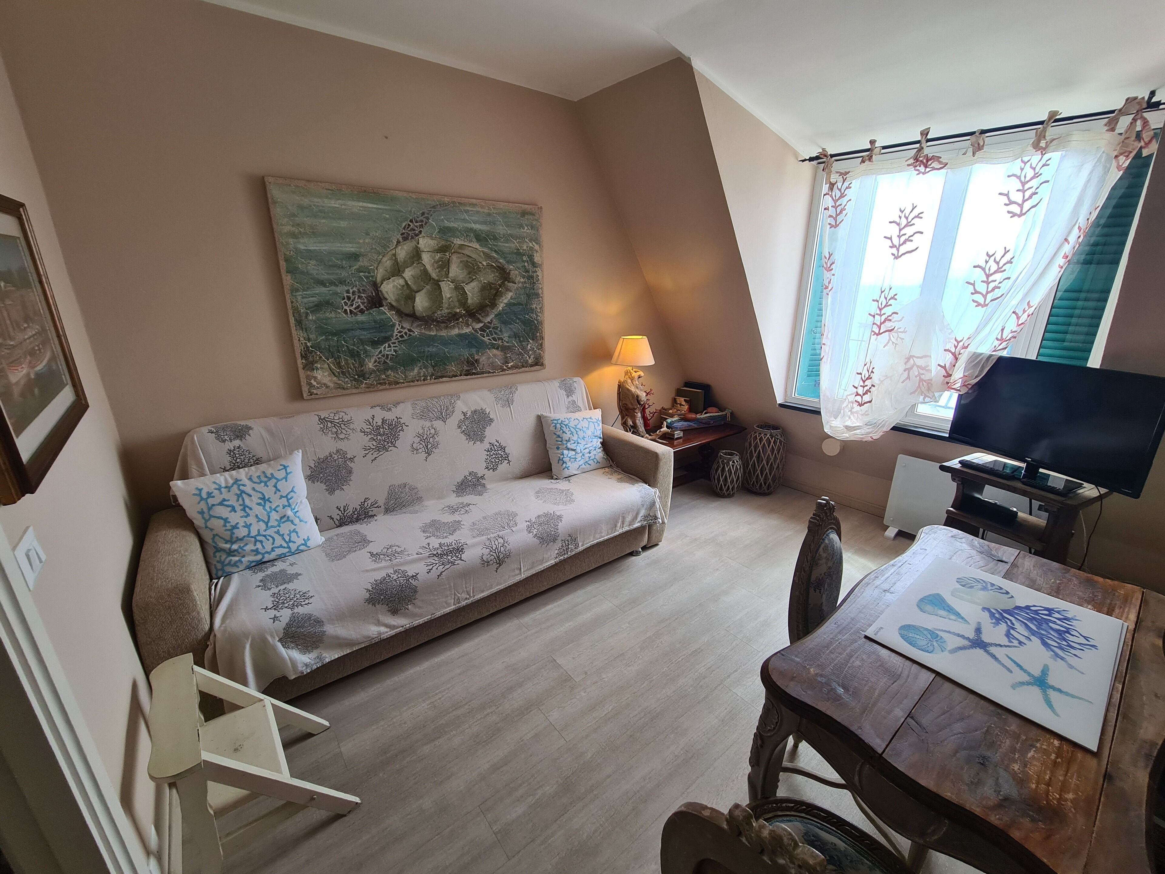 A cozy living room with a sofa, a small table, a TV, and a window with curtains.